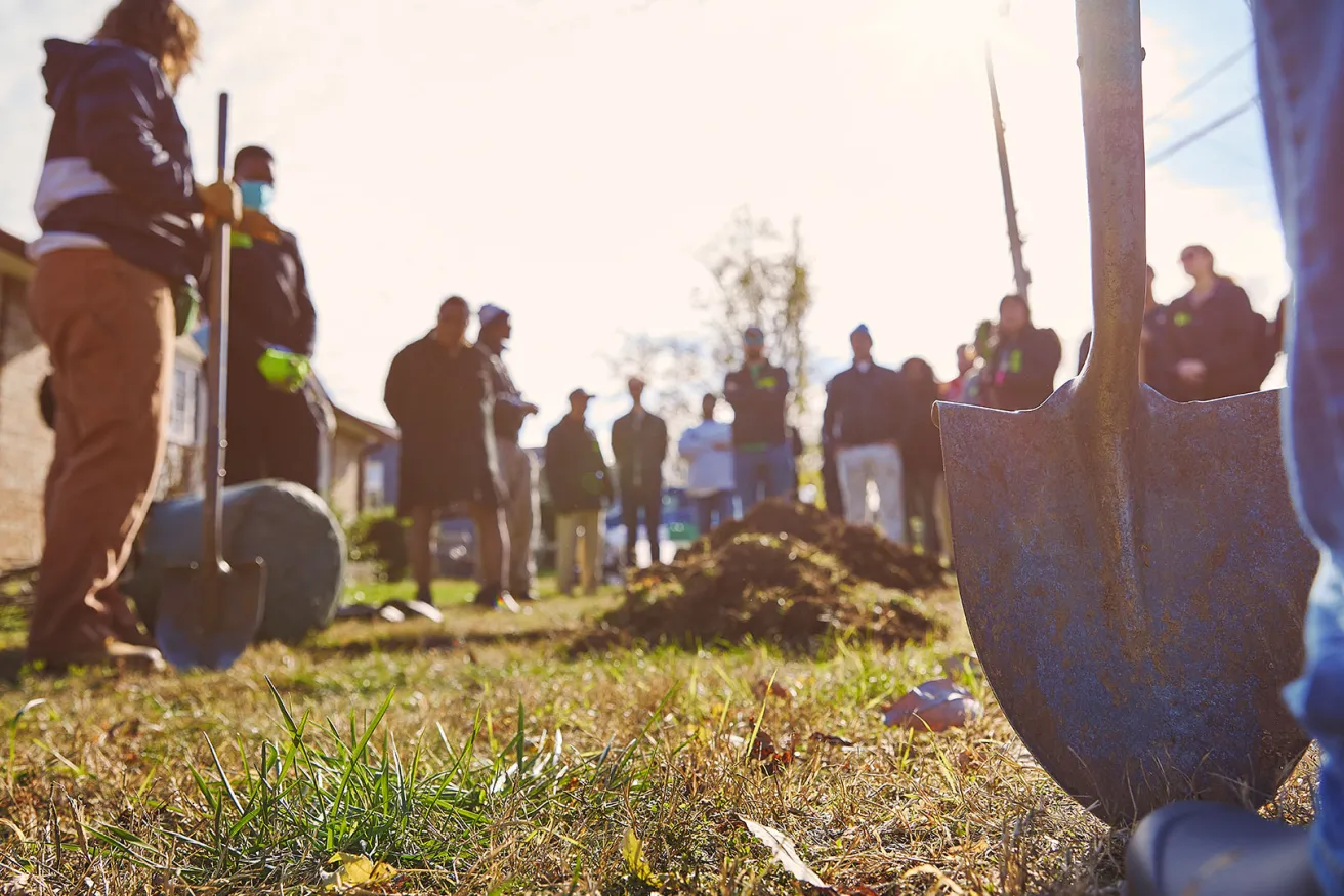 Several people with shovels digging holes in the ground to plant trees.