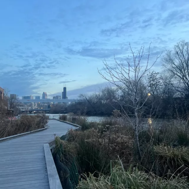 A scenic boardwalk stretches toward a river, flanked by charming buildings in the background.