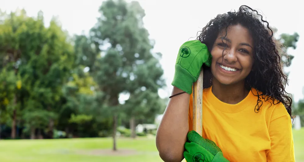 Woman wearing bright green gloves, leaning on her shovel.