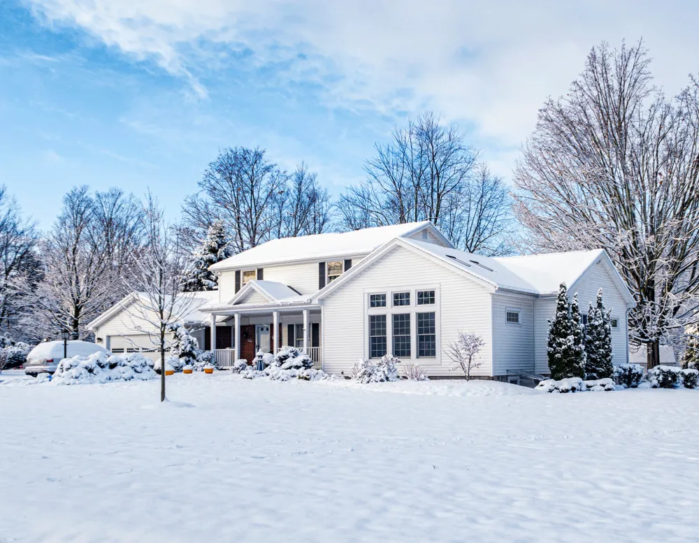 A white house surrounded by snow, illustrating strategic tree planting for warmth and reduced energy bills.