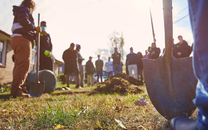 Several people with shovels digging holes in the ground to plant trees.