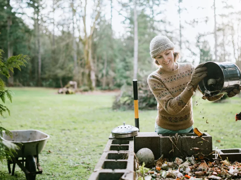 A woman is removing leaves from a compost bin, preparing organic material for composting.