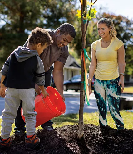 family watering their new tree in the front yard