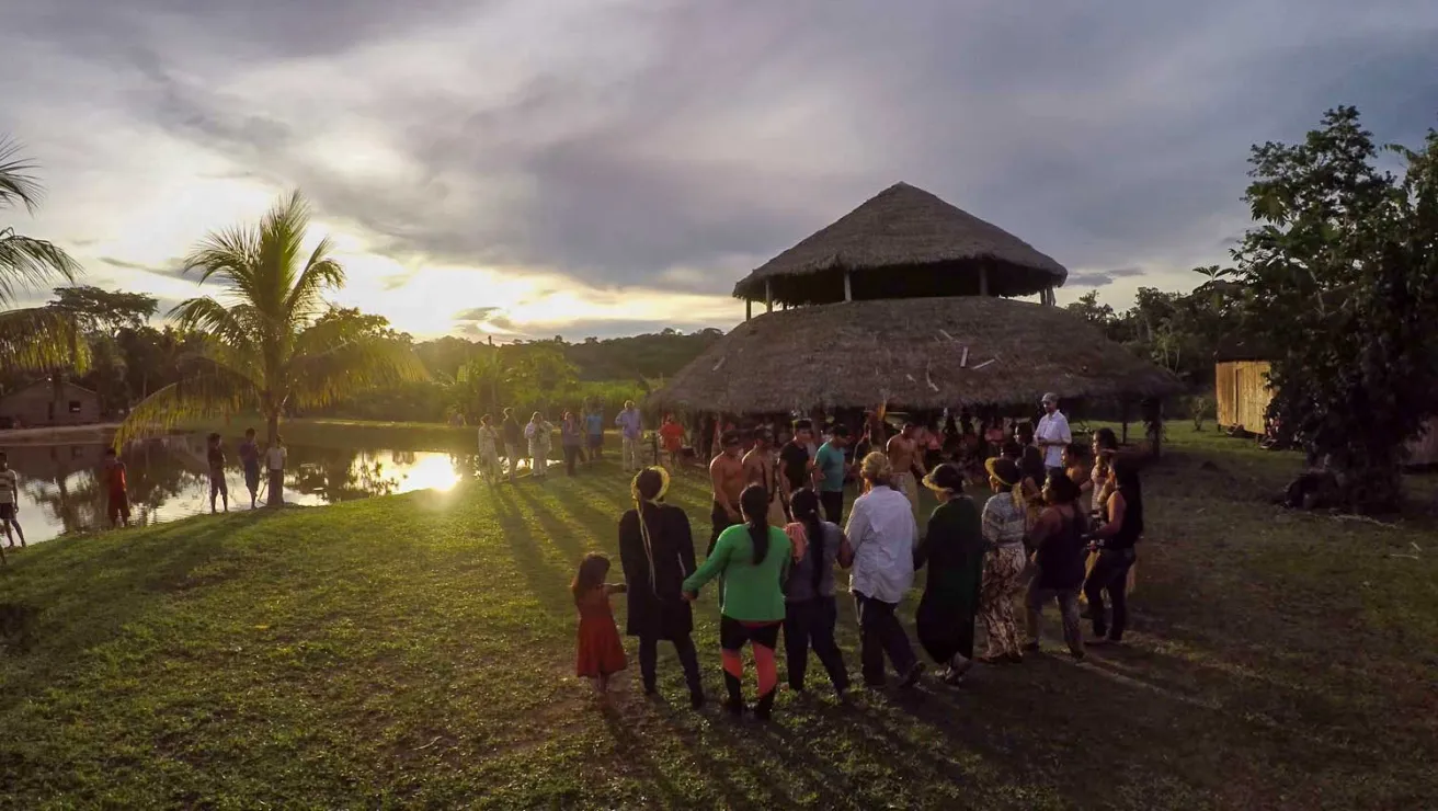 People gathered next to a river, soaking in the beautiful sunset.